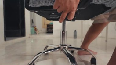 Dönen bir ofis sandalyesinin yanında yerde dinlenen birinin ayaklarının yakın çekim görüntüsü. Sandalye, döşeme döşemesi ile döşenmiş basit bir kapalı ortama karşı dizilmiş bir ağ ve krom tabana sahip..