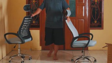 Ahşap kapılı ve döşemeleri döşemeli bir odada modern ergonomik ofis sandalyesini monte eden bir kişi. Sandalye, rahat bir ev ortamı sunan, ayarlanabilir bir başlık ve örgü içeriyor..