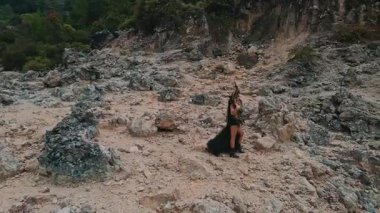 Dramatik siyah kıyafetli bir kadın kayalık bir arazide yürüyor, doğa ve modanın bir karışımını sergiliyor. Sahne bir macera ve gizem hissi yakalıyor..