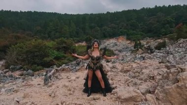 Yeşillik ve ağaçlarla çevrili kayalık arazide süslü bir kostümle dikilen dramatik bir sahne. Gökyüzü bulutlu, manzaraya karamsar bir atmosfer ekliyor..