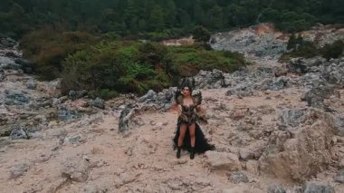 Özenle hazırlanmış bir kostüm içinde, yemyeşil ve volkanik manzaralarla çevrili kayalık arazide duran bir kişinin dramatik bir sahnesi. Bu figür, güçlü bir varlığı somutlaştıran kendine güvenen bir görüntü sergiliyor..