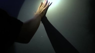 Duvara doğru uzanan bir el loş ışıkta uzun bir gölge bırakıyor. Sahne bir keşif ve merak hissi veriyor..