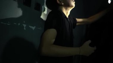 Karanlık bir ortamda, yumuşak bir ışıkla aydınlanmış, düşünceli bir ifadeyle yukarıya bakan bir insan. Elleri nazikçe yüzlerine dokunuyor, dramatik ve içsel bir ruh hali yaratıyor..