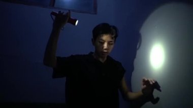 Karanlık bir odada, bir duvarı aydınlatmak için el feneri kullanan biri. Işık odaklanmış bir ışın yaratıyor, gölgeler oluşturuyor ve dokuları renklendiriyor. Atmosfer gizemli ve derin derin..
