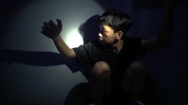 Gölgeli bir figür, yumuşak bir ışık kaynağı tarafından aydınlatılmış karanlık bir duvara karşı duruyor. Atmosfer gergin ve gizemli. Endişe ve entrika hissi uyandırıyor..