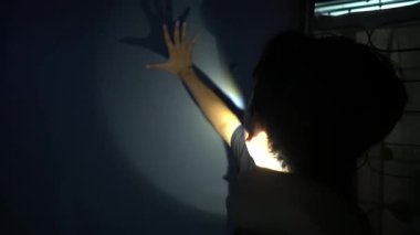 Duvarlarında gölgeler olan loş bir iç mekan. Bir figür kapının önünde çömelmiş gizem ve entrika atmosferi yaratıyor. Ayarlar sessiz ve muhtemelen terk edilmiş bir bölge olduğunu gösteriyor..