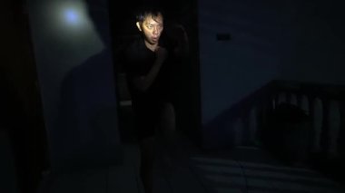 Loş bir koridorda elinde yüzünü aydınlatan bir el feneri tutan bir insan. Çevre karanlık, gizemli bir atmosfer yaratıyor..