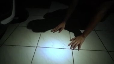 Bir çift el ve bacağın yer aldığı loş bir sahne gizemli ve ürkütücü bir atmosfer yaratıyor. Zemin kiremitli ve bir ışık kaynağı bacakları aydınlatıyor..