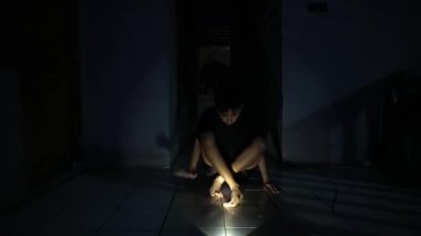 Loş bir odada bağdaş kurup oturan bir insan, elinde zemini aydınlatan bir el feneri tutuyor. Duvarlara gölgeler konuyor, gizemli bir atmosfer yaratıyorlar..