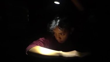 Loş bir odada, kollarına odaklanmış, ışık huzmesi tarafından aydınlatılmış genç bir insan. Işık ve gölge arasındaki zıtlık dramatik bir atmosfer yaratıyor, konsantrasyonu ve iç gözlemleri vurguluyor..