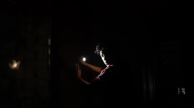 El feneri tutan, küçük bir alanı aydınlatan bir kişinin elini gösteren loş bir sahne. Arka plan çoğunlukla karanlık, gizemli bir atmosfer yaratıyor..