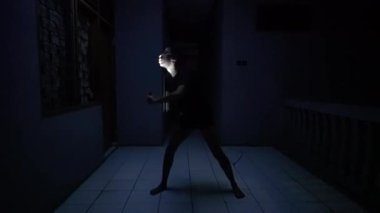 Karanlık bir koridorda fenerle aydınlatılmış dramatik bir poz veren biri. Sahne bir gerilim ve gizem hissi veriyor, gölgeler atmosferi güçlendiriyor..