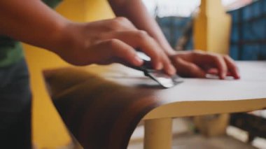 Ahşap bir yüzeyi zımparalayan, el işçiliği ve detaylara dikkat çeken birinin yakın çekimi. Arkaplanda sıcak renkler var, samimi bir atölye ortamı izlenimi veriyor..