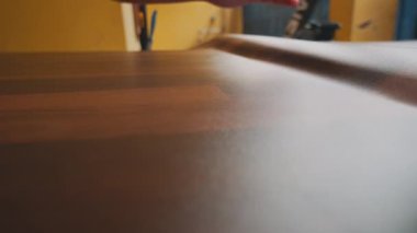 Ahşap bir yüzeyi düzleştiren, ahşap dokusunu ve tahtalarını gösteren yakın plan bir el görüntüsü. Arka plan bulanık ve ahşap işçiliğinde kullanılan işçiliği vurguluyor..