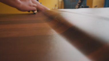 Ahşap bir yüzey üzerinde kazıyıcı kullanan, marangozluk ve ahşap işçiliğindeki detaylara dikkat eden bir kişinin yakın çekimi..