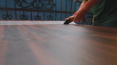 Arka planda dekoratif korkuluk bulunan tahta bir masa üzerindeki malzemeyi kesmek için bıçak kullanan bir kişi. Odak noktası eller ve kesme eylemi..