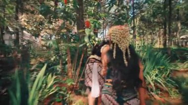 Aralarında karmaşık başlıklar ve batik eteklerin de yer aldığı geleneksel Endonezya kostümleri giymiş iki sanatçı, canlı, güneşli bir orman bahçesinde el ele yürüyorlar. Çekim arkalarından geliyor, güzel kıyafetlerini sergiliyor..