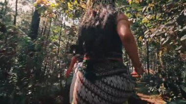 Gösterişli, geleneksel Endonezya kıyafeti giymiş iki kişi yemyeşil orman ortamında kameradan el ele yürüyorlar. Güneş ışığı ağaçların arasından süzülerek büyülü ve romantik bir atmosfer yaratır..