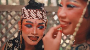 Dramatik, geleneksel Cava makyajlı, Rama karakterini canlandıran bir erkek oyuncunun yakın çekimi. Ön planda yumuşak odaklı olan ortağıyla sevgiyle gülümser ve etkileşim kurar..