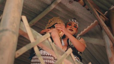 Düşük açılı bir çekim, geleneksel kostümlü bir Cava çifti arasındaki dramatik ve samimi anı yakalar. Adam işaret eder ve sessizce işaret eder, ortak bir sır ya da hikaye önerir..