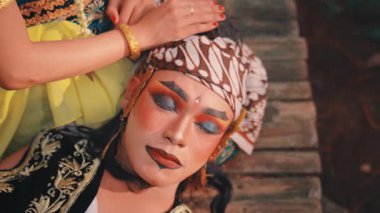 Kafasını dinlendiren özenle hazırlanmış makyajlı bir Cavalı sanatçının tepeden tırnağa sanatsal görüntüsü. Ortağının elleri, altın takılarla süslenmişti, onu nazikçe rahatlatırdı. Kültürel ayrıntı ve duyguyla dolu bir sahne..