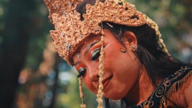 Nazik, sakin bir gülümsemesi olan güzel bir Cava 'lı kadın sanatçı profili. Çekim, onun altın başlığının, makyajının ve geleneksel kostümünün karmaşık detaylarını bulanık doğal bir arka plana karşı vurguluyor..