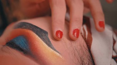 Aşırı yakın plan bir kadının parmaklarını kırmızı tırnak cilasıyla yakalıyor. Geleneksel Cava performansı makyajıyla bir erkeğin alnını nazikçe okşuyor. Sanatın detaylarını ve samimi jestini vurguluyor..