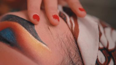 Sanatsal, aşırı yakın plan bir kadının elini kırmızı tırnak cilasıyla yakalıyor ve geleneksel Java makyajı ve batik başörtüsü takan bir adamın alnını nazikçe okşuyor. Güçlü bir özen ve samimiyet sembolü..