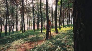 Geleneksel bir Cava ya da kabile okçusu gibi giyinmiş elinde ok ve yay tutan bir adam, güneşli bir çam ormanında çıplak ayakla yürüyor. Sahne, tarih, folklor ve macerayı çağrıştırıyor..