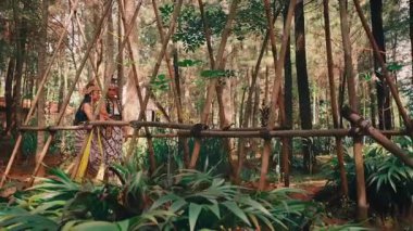 Geleneksel giyinmiş bir Java çifti çam ormanında kırsal bambu çitlerinin yanında yan yana duruyor. Sahne huzurlu ve romantiktir. Doğada eski bir folklor ve yaşam hissi uyandırır..