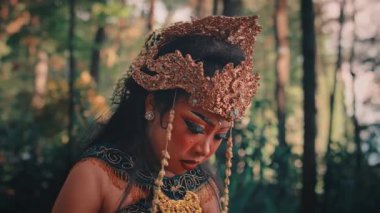 Ormandaki kadın bir Cava müzisyeninin güzel bir orta boy resmi. Süslü bir kostüm ve başlık giyip etrafa bakınırken duygusal ve endişeli bir ifade takınıyor..