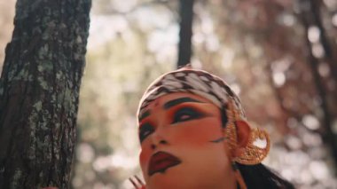 Dramatik makyajı ve süslü altın kulaklığı olan geleneksel bir Cava okçusunun yakın çekimi. Etrafına ciddi ve tetikte bir ifadeyle bakıyor, sanki mistik ormanda avlanıyor ya da arıyor gibi..