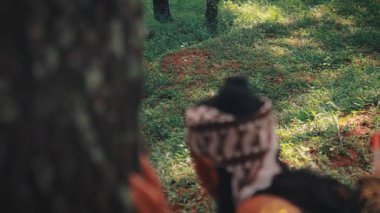 Omzunun üstünden çekilen bir fotoğrafta geleneksel bir Cava okçusunun ağacın arkasına saklanıp ormana baktığı görülüyor. Bu bir şüphe, gizlilik ve gözlem hissi yaratır, sanki avlanmak ya da tehlikeden saklanmak gibi..