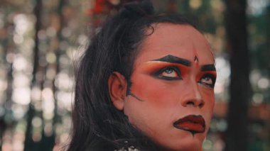 Dramatik makyajlı ve geleneksel kostümlü bir Cava 'lının sanatsal yakın çekimi. Bir ormanda, Endonezya folklorundan güçlü bir karakteri canlandırırken ciddi ve yoğun bir ifadeyle kafasını kaldırıyor..