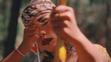 Tiyatro makyajlı, ok ve yay hedefleyen bir Cava okçusunun yoğun yakın çekimi. Onun kararlı ifadesi ve geleneksel silahının ayrıntıları üzerinde duruluyor. Folklordan bir savaşçı tasvir ediliyor..