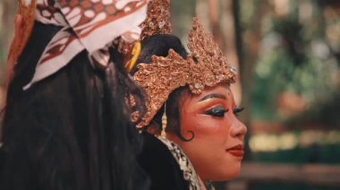 Yakın çekim, geleneksel kostümlü bir Cava çifti arasındaki samimi ve nazik anı yakalar. Altın başlıklı kadın, eşinin yüzüne dokunurken ona sevgiyle bakıyor..