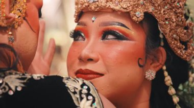 Özenle hazırlanmış altın başlıklı ve dramatik makyajlı geleneksel bir Java dansçısının güzel bir yakın çekimi, bir orman ortamında partneriyle samimi ve duygusal bir anı paylaşıyor..