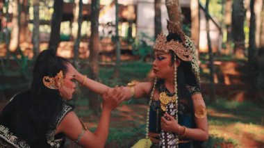 Geleneksel kostümlü ve makyajlı iki Java dansçısı arasında dokunaklı bir sahne. Bir dansçı diğerini rahatlatır. Diz çöküp ormandaki dramatik ve duygusal bir anı tasvir eder..