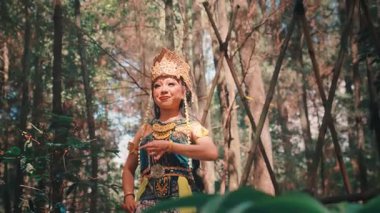 Büyüleyici altın başlıklı ve geleneksel kostümlü güzel bir Cava dansçısı Endonezya kültür mirasını sergileyen sakin bir ormanda zarif ve zarif bir dans sergiliyor..