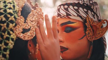 Geleneksel bir Cava erkek dansçısının partnerinin yüzüne nazikçe dokunduğu hassas ve duygusal bir anı yakalayan yakın çekim. Makyaj, kostüm ve sevgi dolu jestlere odaklanıyoruz..