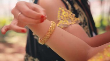 Dişi bir Cava dansçısının sanatsal yakın çekimi. Çekim, geleneksel dans için gerekli zarif, sembolik el hareketlerini (mudra), altın bileziği ve kırmızı tırnakları vurgular.