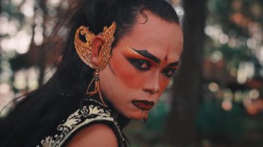 Bir Cava erkek dansçısının aşırı yakın çekimi. Dramatik geleneksel makyaj ve altın kulaklı aksesuar ile süslenmiş yüzü, kameraya güçlü bir bakışla bakarken çerçeveyi dolduruyor..