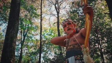 Endonezya folklorundan bir kahramanı temsil eden metanetli erkek bir Cava dansçısı yayını tamamen çekerek yukarıya nişan alıyor. Odaklanmış duruşu, geleneksel bir savaşçının gücünü ve becerisini temsil ediyor..