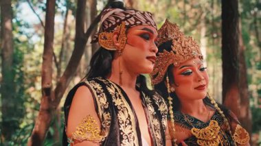 Geleneksel bir Cava çiftinin güzel bir yakın çekimi. Süslü, altın başlıklı kadın, başını partnerinin omzuna dayar, ormanda hassas ve samimi bir anı paylaşır..