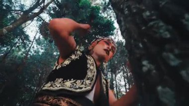 Alçak açıdan bakıldığında, geleneksel kostümlü bir Java erkek dansçısı duygusal ve anlamlı bir dans sergiliyor, büyük bir ağaca yaslanıyor ve onunla etkileşime geçiyor, doğayla derin bir ruhsal bağı simgeliyor..