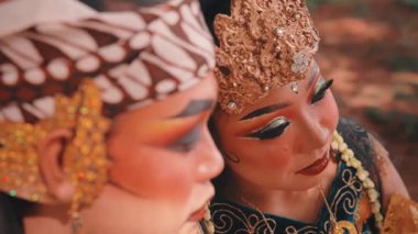 Süslü makyajlı ve altın başlıklı kadın bir Cava dansçısının samimi, omuz üstü yakın çekimi. Sevgi ve dinginlik gösterisi yaparak başını partnerine doğru eğmiş..