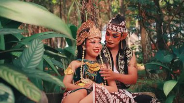 Zengin bir ormanda geleneksel bir Java çiftinin mutlu ve romantik bir sahnesi. Erkek dansçı neşeyle eşinin çenesine ve yüzüne dokunur, onu güldürür ve güldürür saf bir sevinç ve şefkat anında.