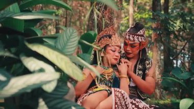 Geleneksel bir Cava çifti ormanda otururken hassas ve romantik bir anı paylaşıyor. Süslü kostümler içinde birbirlerine sevgi ve sevgiyle bakıyorlar. Nazikçe el ele tutuşuyorlar..