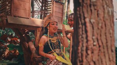 İki geleneksel Cava dansçısı, bir erkek ve bir kadın, ormanın bir ağaç evinde, neşeli ve mutlu bir sahnede birlikte gülüp sohbet ediyorlar..