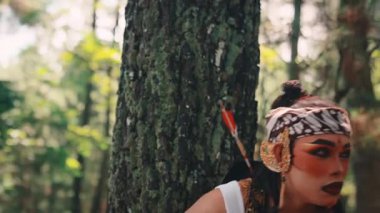 Geleneksel okçu rolünde bir Cava dansçısı bir ağacın arkasından ortaya çıkar. Tedbirli bir ifade ve dramatik bir makyajla poz vermeden önce dikkatli bir şekilde ormanı inceler..